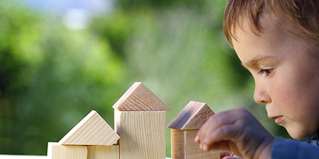 boy raises his hand to the house from wooden cubes